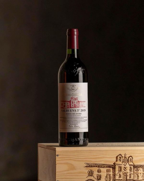 Vega Sicilia Valbuena 2019 bottle on a wooden wine case against a dark background